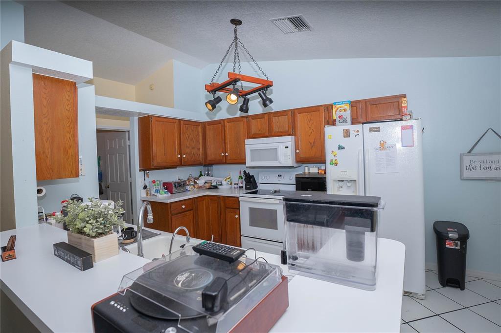A kitchen features wood cabinets, white appliances, a breakfast bar, and a hanging light fixture — 2773 WOODSTREAM CIRCLE, KISSIMMEE, FL