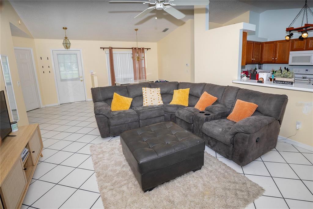 A living room with a large gray sectional, ottoman, and tile flooring, opening to a kitchen — 2773 WOODSTREAM CIRCLE, KISSIMMEE, FL
