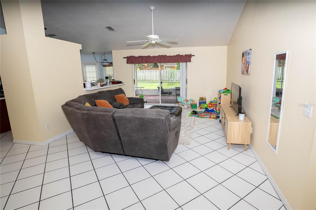 A living room features a gray sectional sofa, tile flooring, and sliding glass doors to outside — 2773 WOODSTREAM CIRCLE, KISSIMMEE, FL