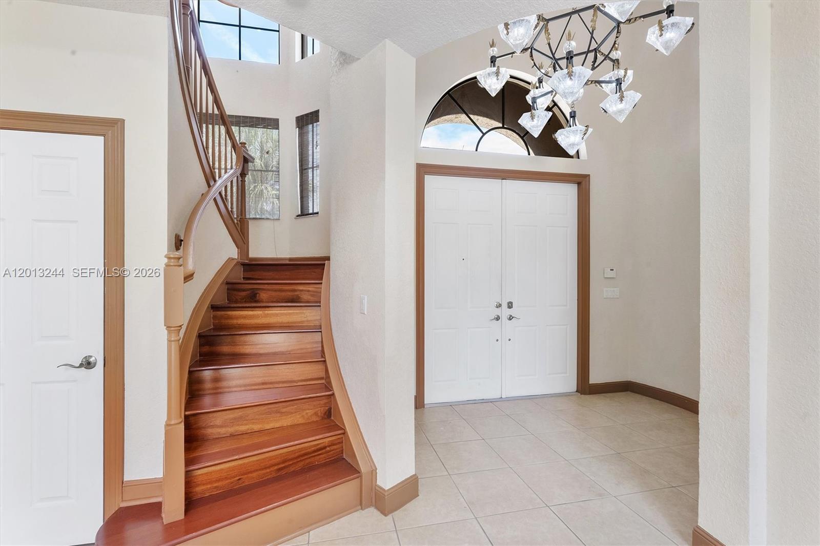 A foyer features a curved wooden staircase, tile flooring, and a large modern chandelier — 10364 Trianon Pl, Wellington FL 33449, WELLINGTON, FL