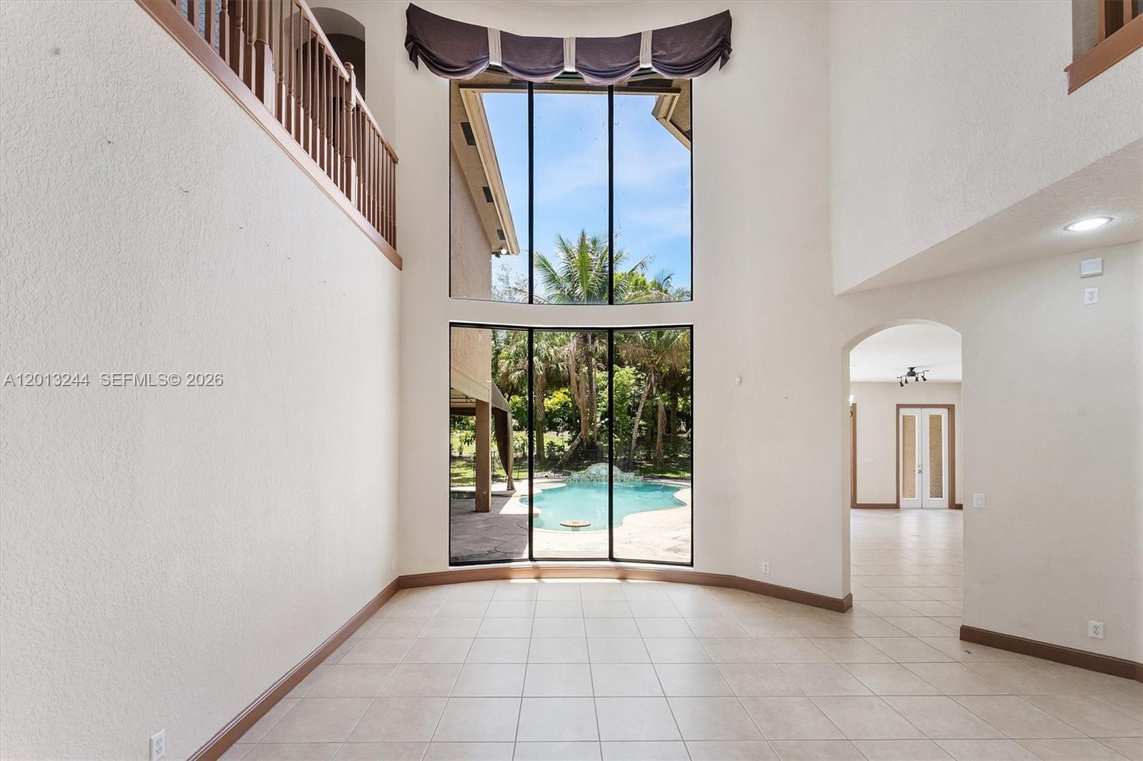 A two-story living room with tile flooring, a large window wall, and pool views — 10364 Trianon Pl, Wellington FL 33449, WELLINGTON, FL