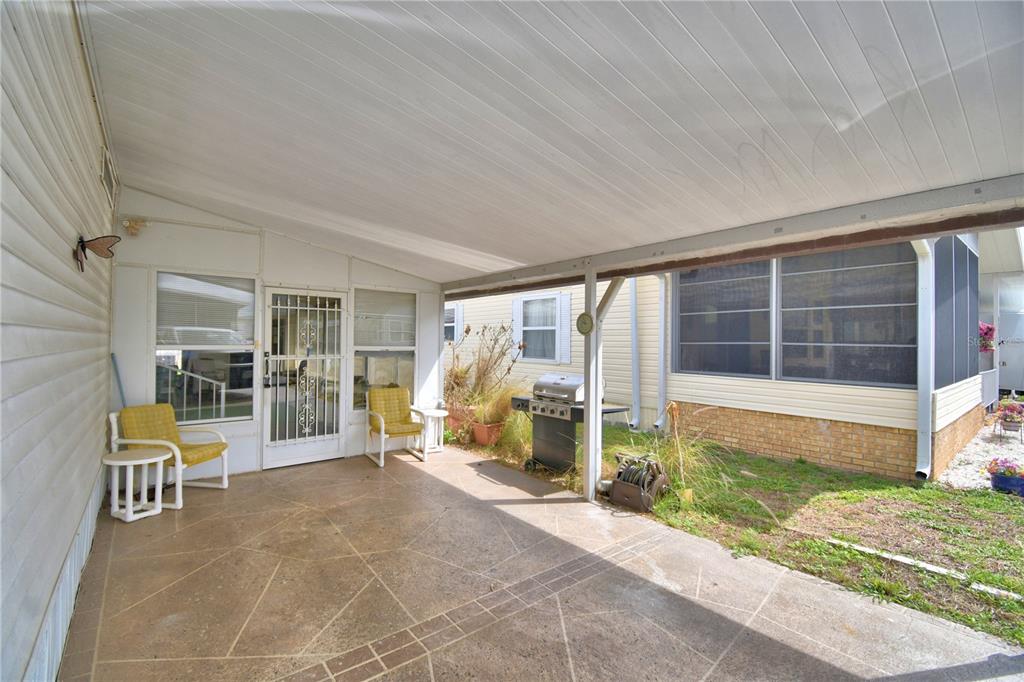A covered concrete patio features two yellow chairs, a grill, and a side entrance door — 4155 SPRUCEWOOD STREET, WINTER HAVEN, FL