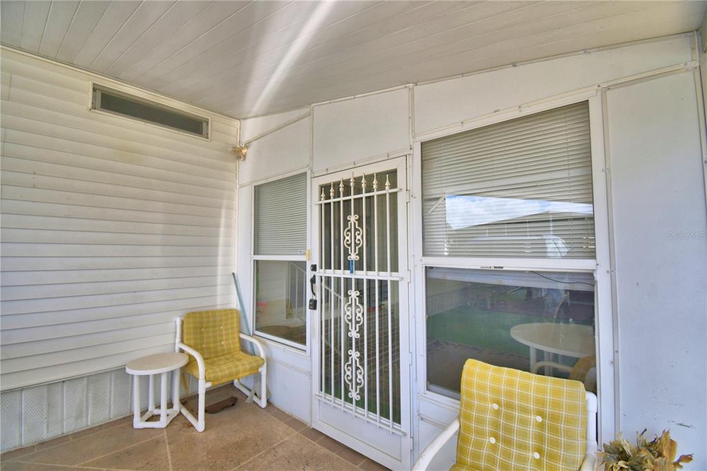 A covered patio features a white security screen door, two yellow chairs, and siding — 4155 SPRUCEWOOD STREET, WINTER HAVEN, FL