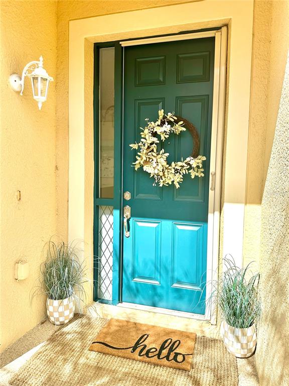 A teal front door with a wreath and a hello doormat sits between two potted plants — 8137 PONKAN ROAD, LAND O LAKES, FL