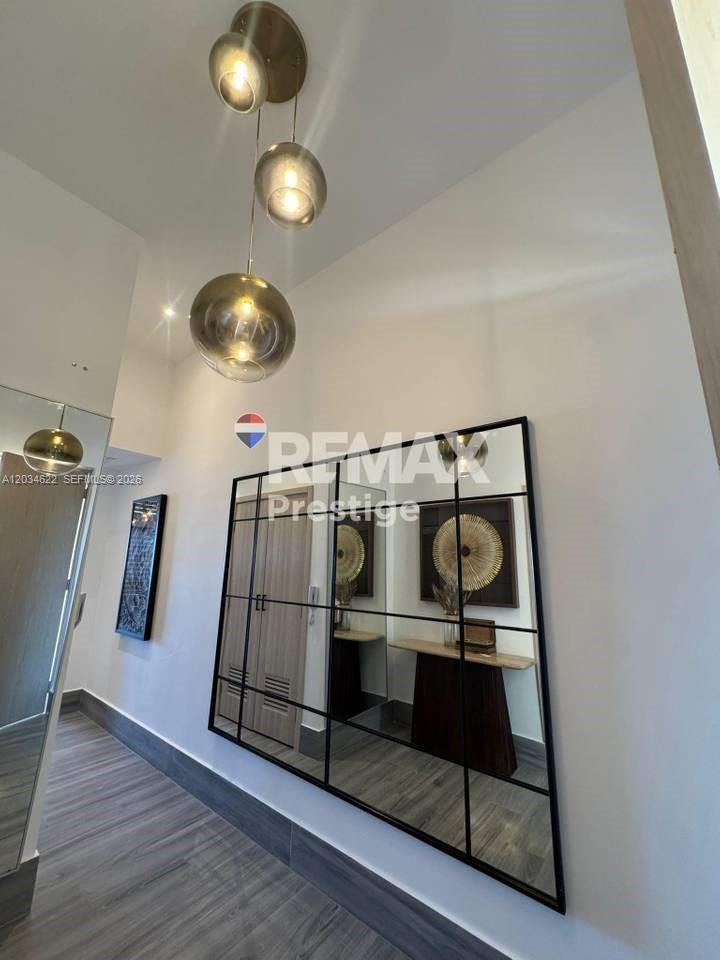 A modern entryway features a grid-style wall mirror, wood-look flooring, and a three-light pendant fixture — 1 Vista alta # 1, FL