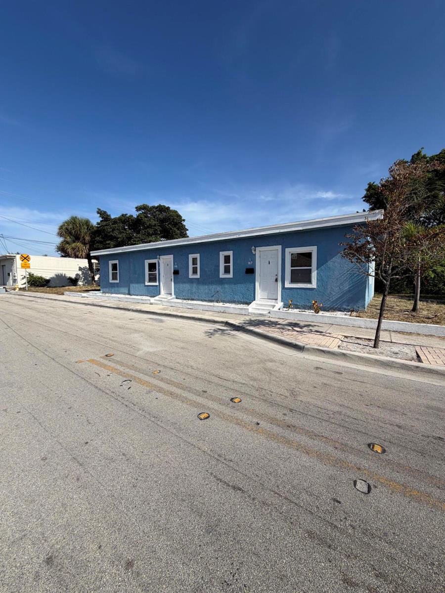A blue, single-story multi-unit building sits along a paved street under a clear sky — 1117 3rd Avenue N # 1, FL 33460, FL