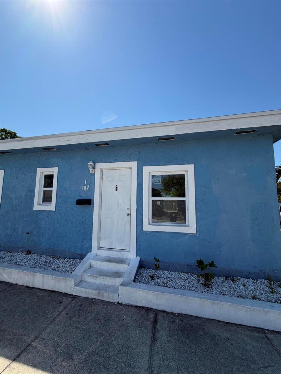 A blue exterior wall features a white front door, two windows, and a concrete step — 1117 3rd Avenue N # 1, FL 33460, FL