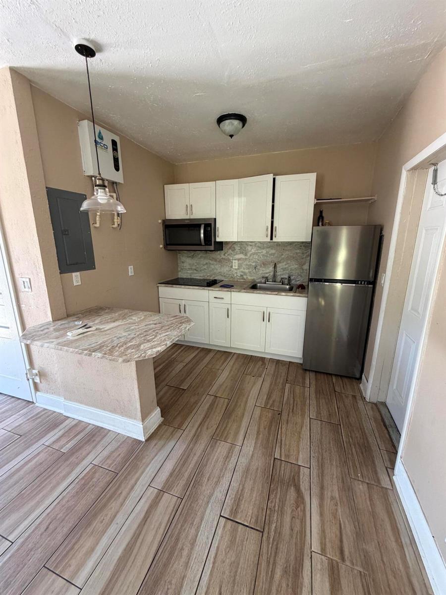 A small kitchen features white cabinets, stainless steel appliances, and a marble-patterned peninsula countertop — 1117 3rd Avenue N # 1, FL 33460, FL