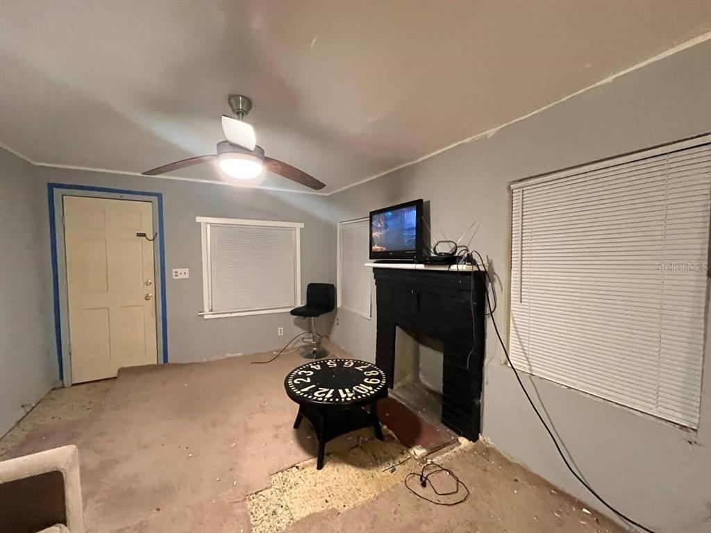 A room with gray walls, a black fireplace, a ceiling fan, and unfinished flooring — 2432 SW 1ST ST, OCALA, FL