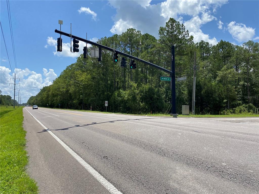 A traffic signal hangs over a paved road at an intersection near a wooded area — Corner of N Main St and NE 53RD AVENUE, GAINESVILLE, FL