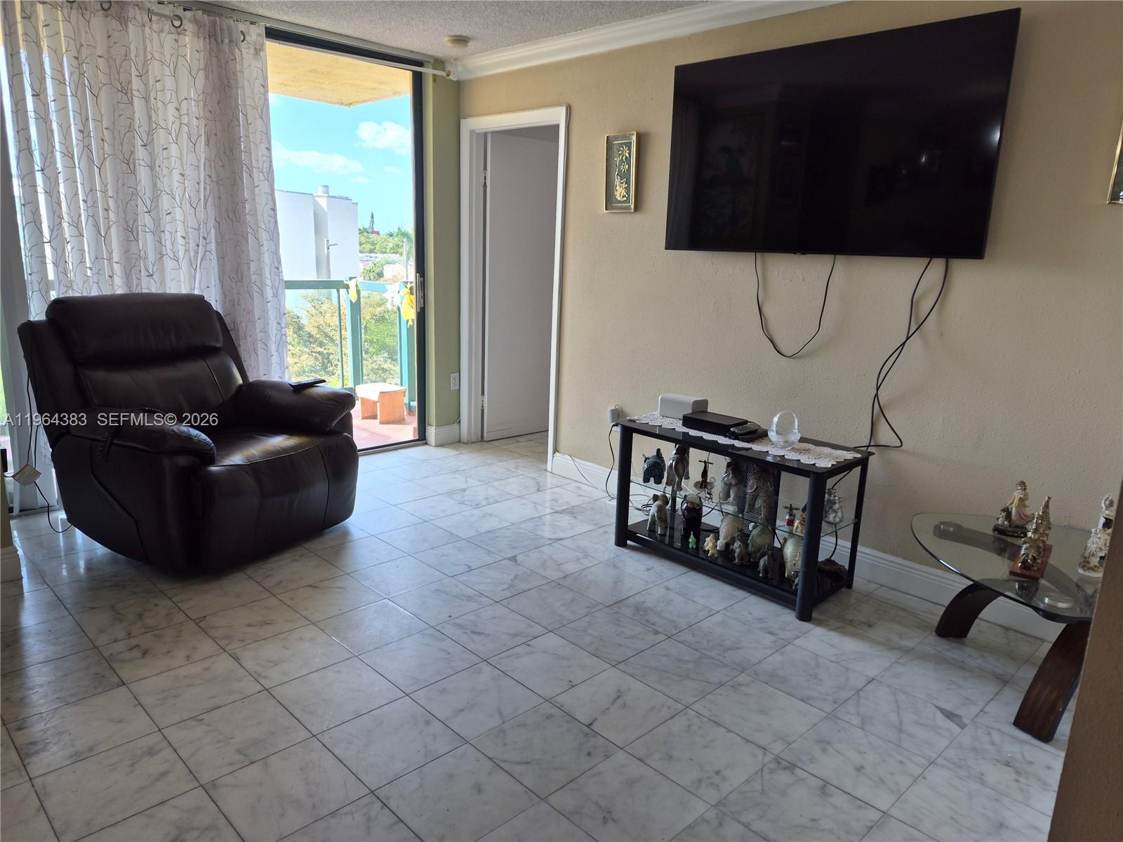 A living room features a dark leather recliner, a wall-mounted television, and marble tile flooring — 11800 SW 18th St # 4, Miami FL 33175, MIAMI, FL