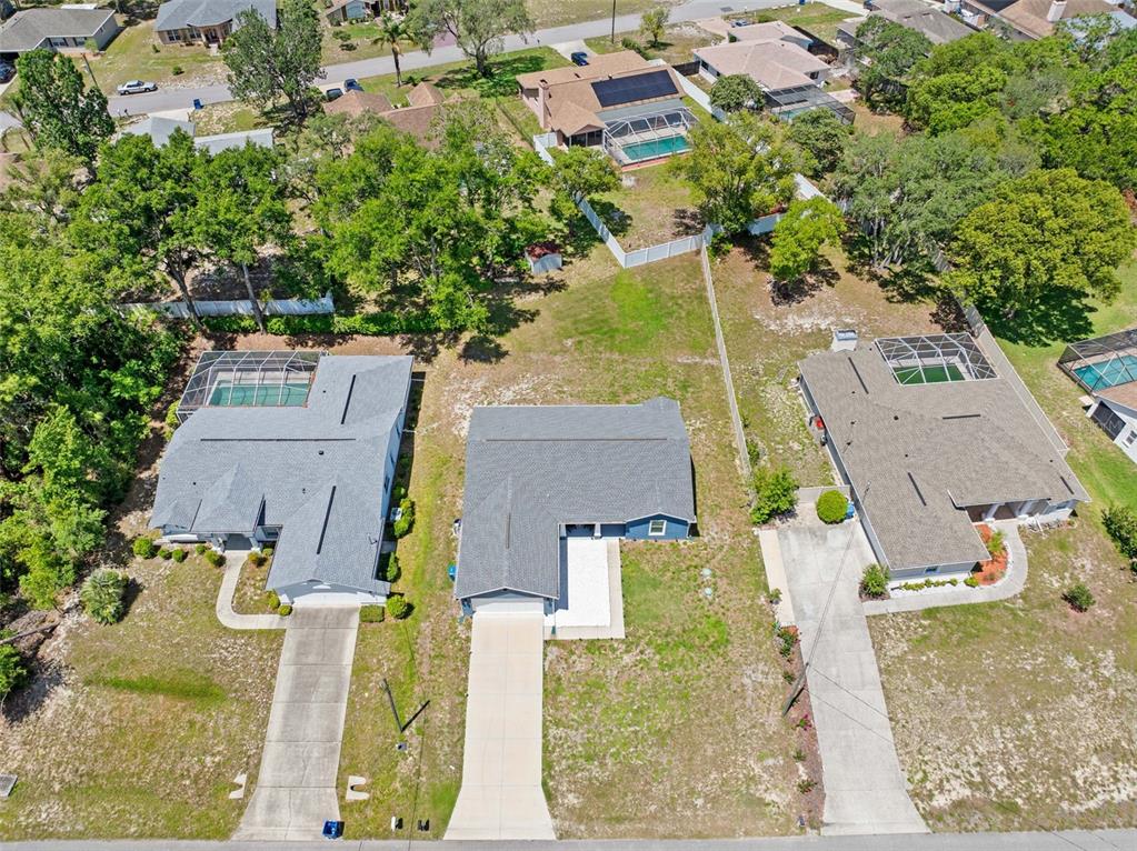 An aerial view shows three suburban houses with driveways and swimming pools on a grassy lot — 2225 RING ROAD, SPRING HILL, FL