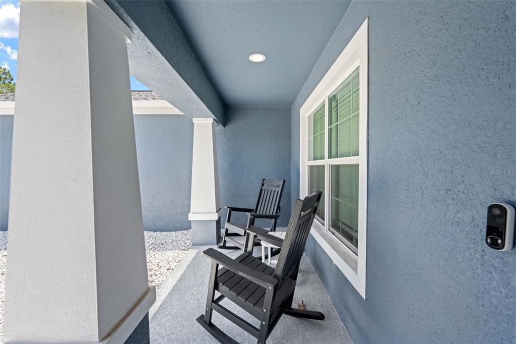 A covered front porch features blue stucco walls, two black rocking chairs, and white columns — 2225 RING ROAD, SPRING HILL, FL