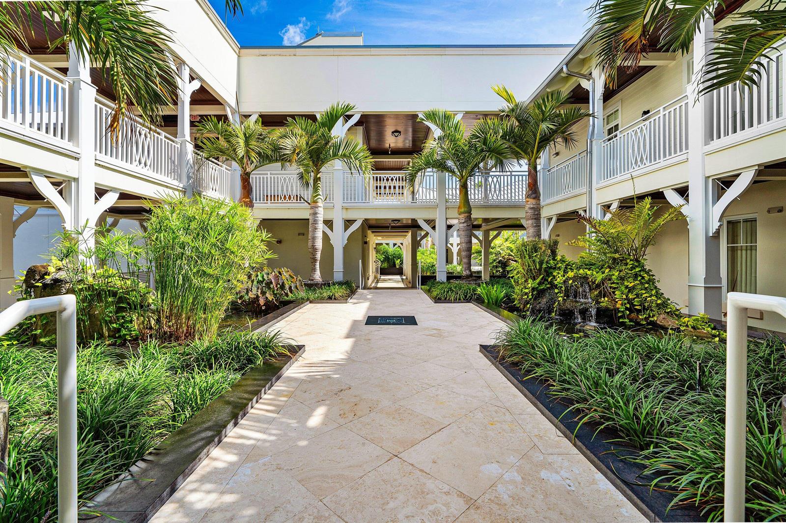 A paved walkway leads through a lush courtyard between two white buildings with covered balconies — 400 S Ocean Boulevard # 105, Delray Beach FL 33483, DELRAY BEACH, FL