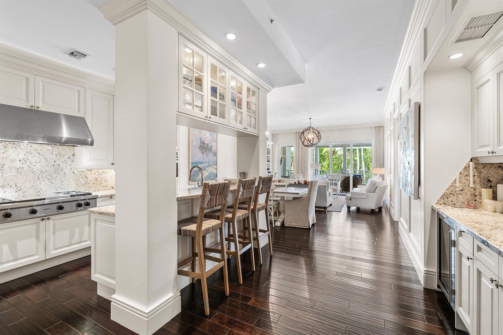 A white kitchen with granite countertops, bar seating, and dark wood floors opens to living — 400 S Ocean Boulevard # 105, Delray Beach FL 33483, DELRAY BEACH, FL