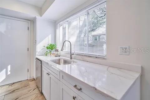 A kitchen features white cabinets, a marble-look countertop, a stainless steel sink, and a window — 11713 RAINTREE DRIVE, TAMPA, FL