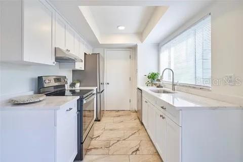 A bright kitchen features white cabinets, stainless steel appliances, and light-colored tile flooring — 11713 RAINTREE DRIVE, TAMPA, FL