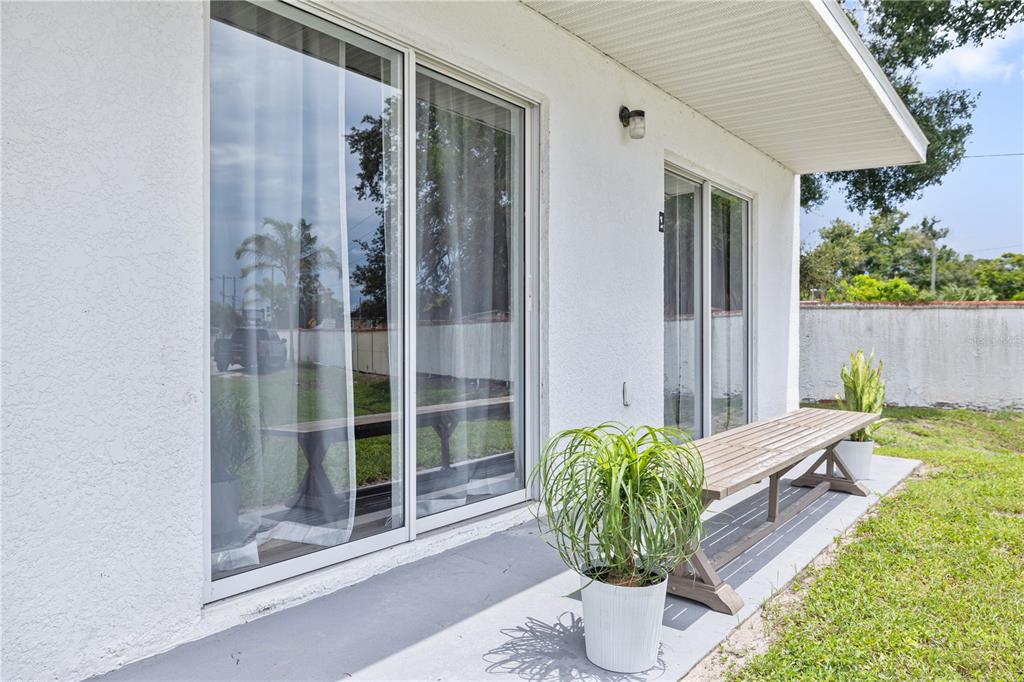 A white exterior wall features two sliding glass doors, a wooden bench, and a potted plant — 9415 CITRUS GLEN PLACE, TAMPA, FL