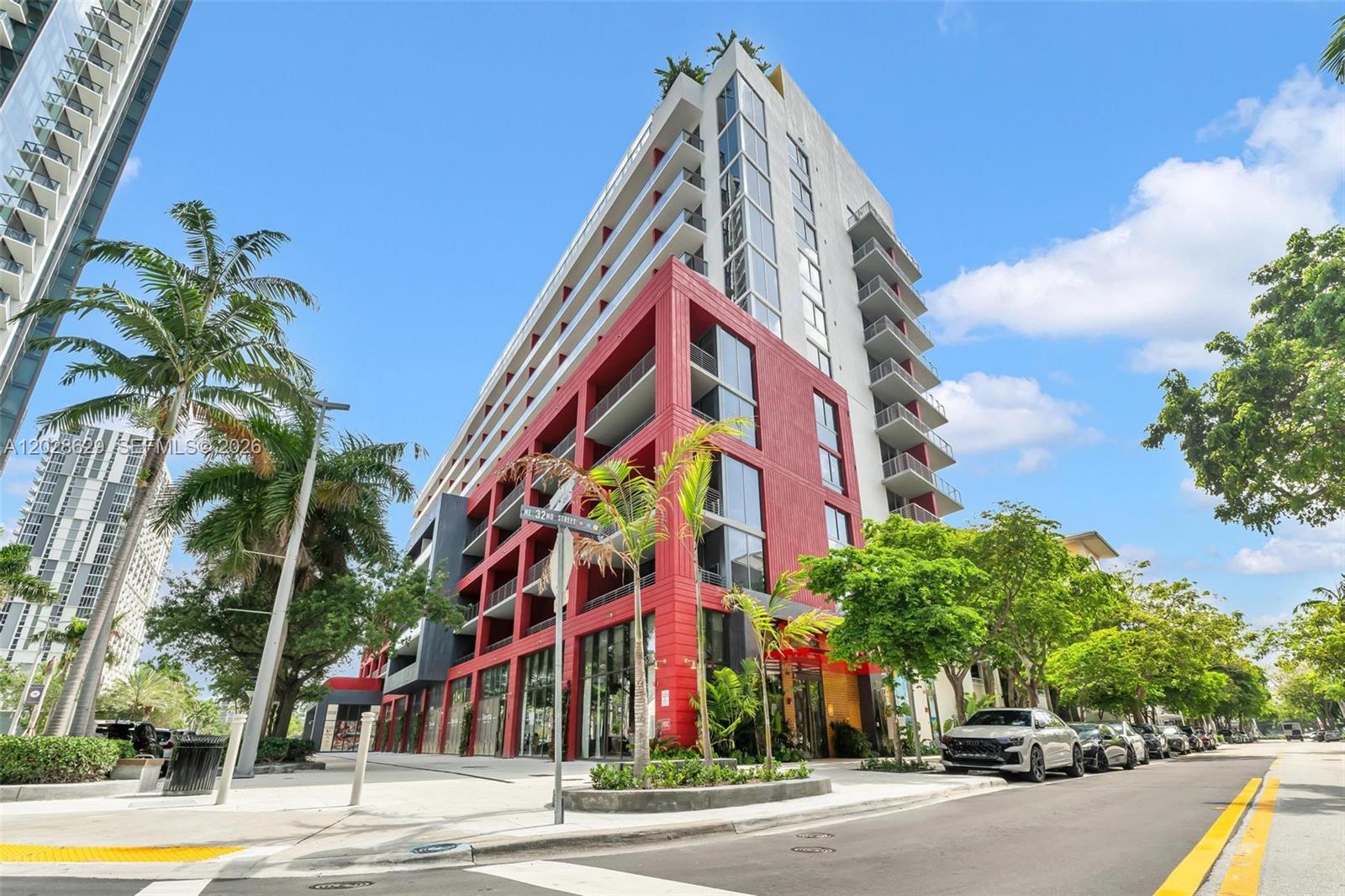 A modern multi-story apartment building features a red facade, balconies, and ground-level storefronts — 90 32nd ST # 909, Miami FL 33127, MIAMI, FL