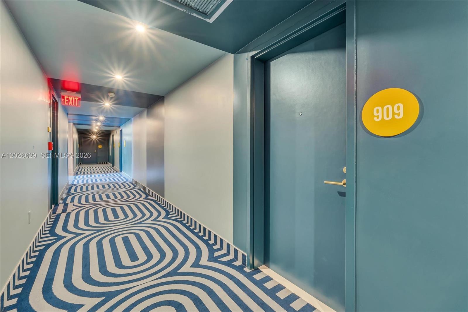 A hallway with blue walls, a patterned carpet, and a door labeled 909 — 90 32nd ST # 909, Miami FL 33127, MIAMI, FL