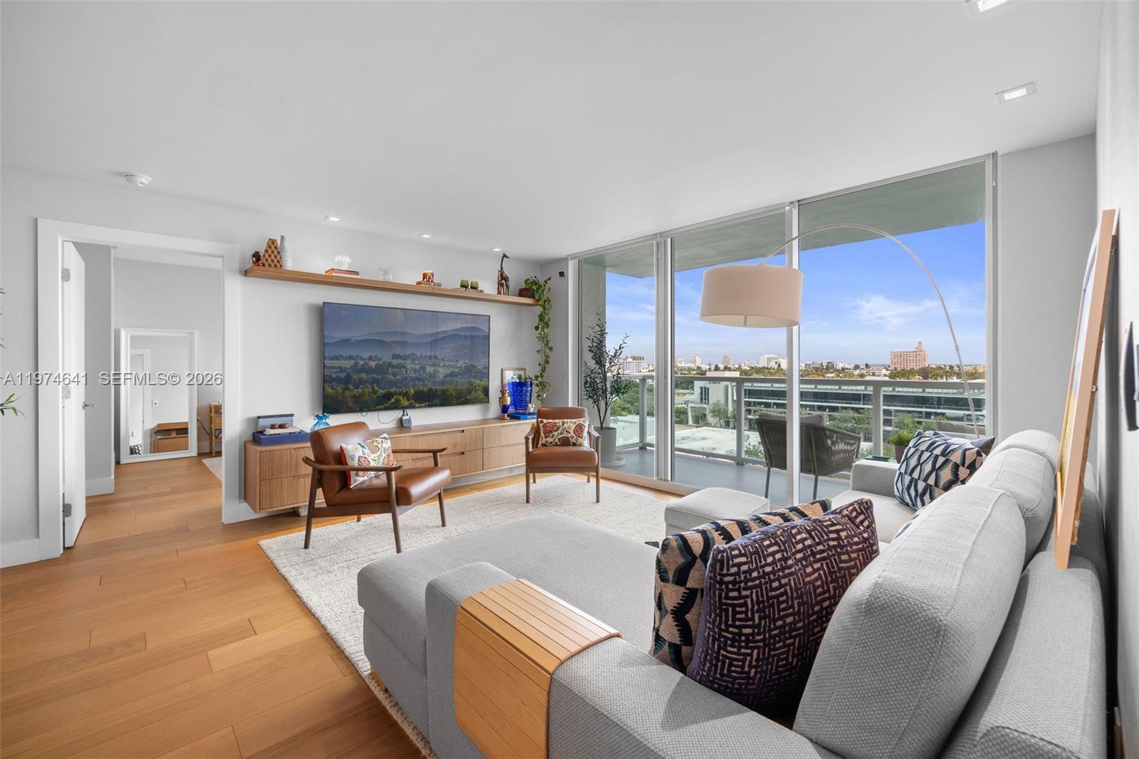 A modern living room features a large sectional sofa, wood media console, and floor-to-ceiling windows — 650 West Ave # 908, Miami Beach FL 33139, MIAMI BEACH, FL