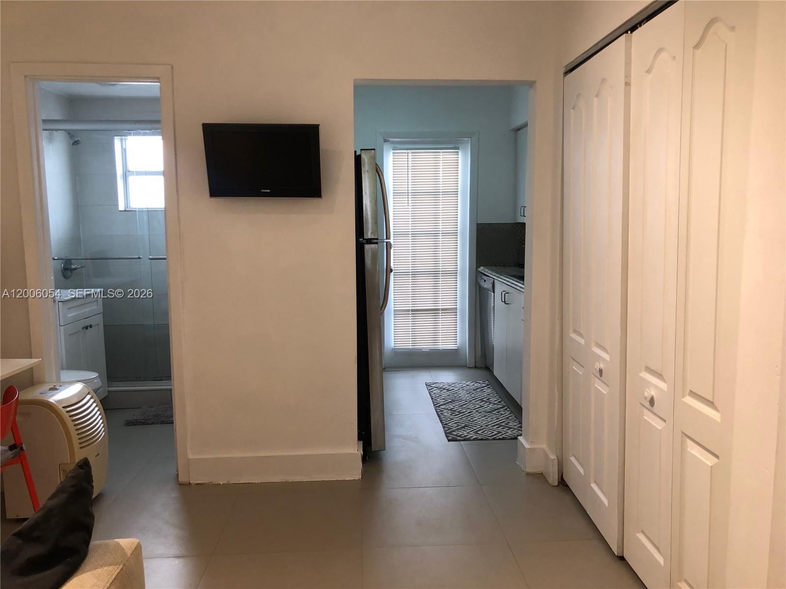 A view of a bathroom, a kitchen with a refrigerator, and white closet doors — 911 Meridian Ave # 105, Miami Beach FL 33139, MIAMI BEACH, FL