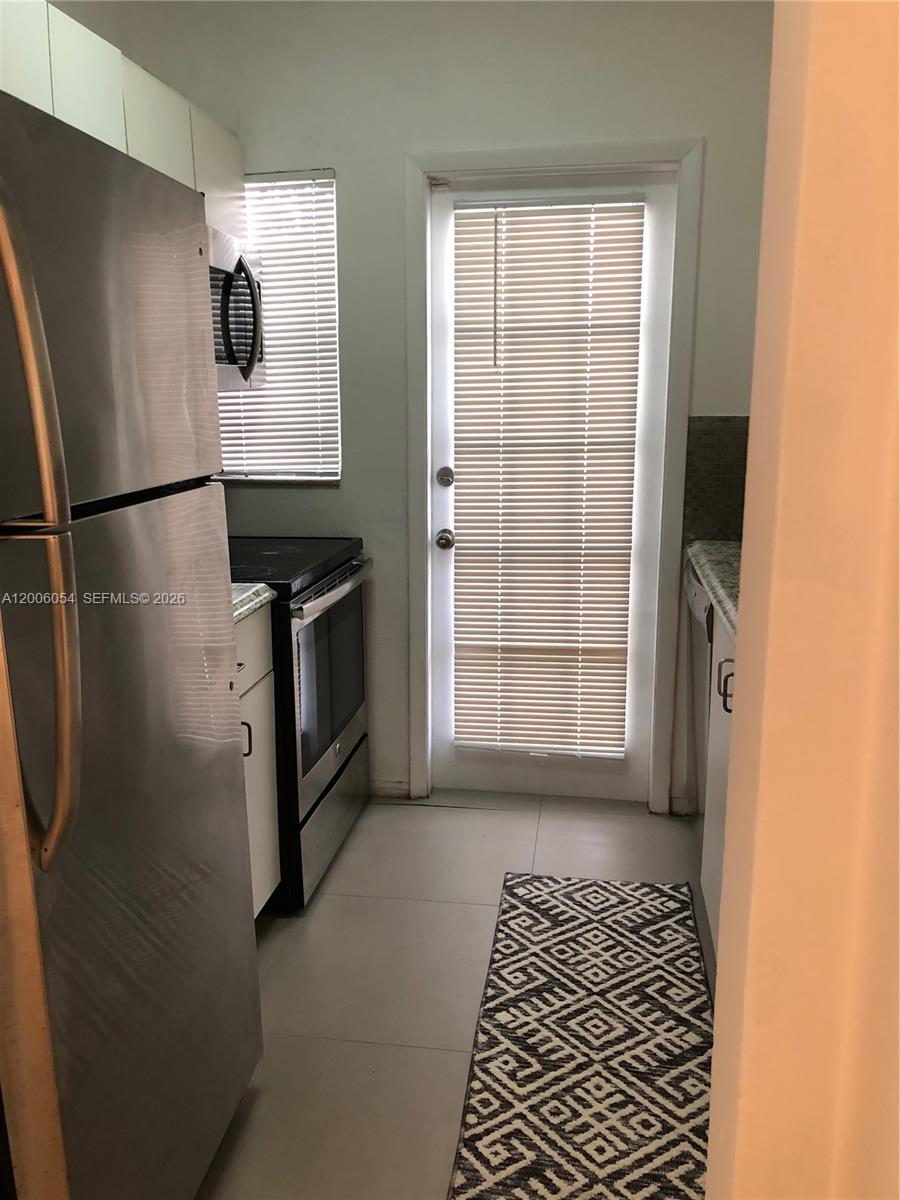 This kitchen features stainless steel appliances, white cabinets, light tile flooring, and a glass-paneled door — 911 Meridian Ave # 105, Miami Beach FL 33139, MIAMI BEACH, FL