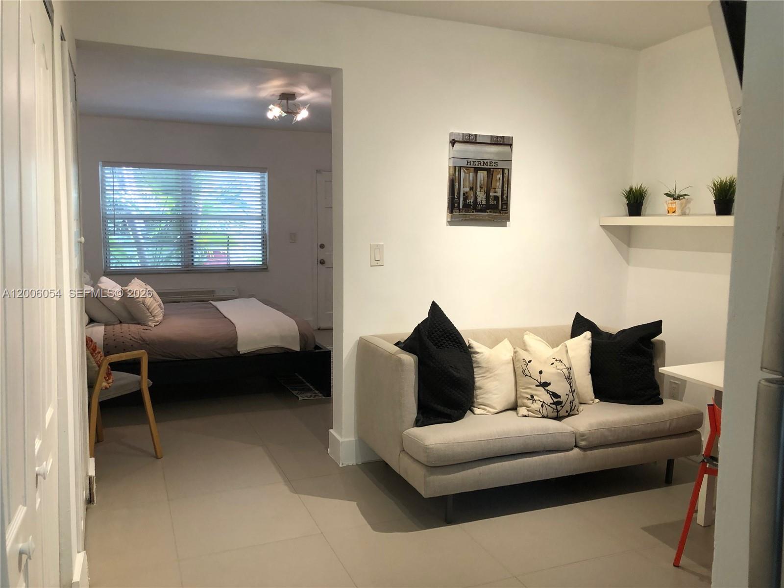 A living area with a sofa and wall shelf opens into a bedroom with tile floors — 911 Meridian Ave # 105, Miami Beach FL 33139, MIAMI BEACH, FL