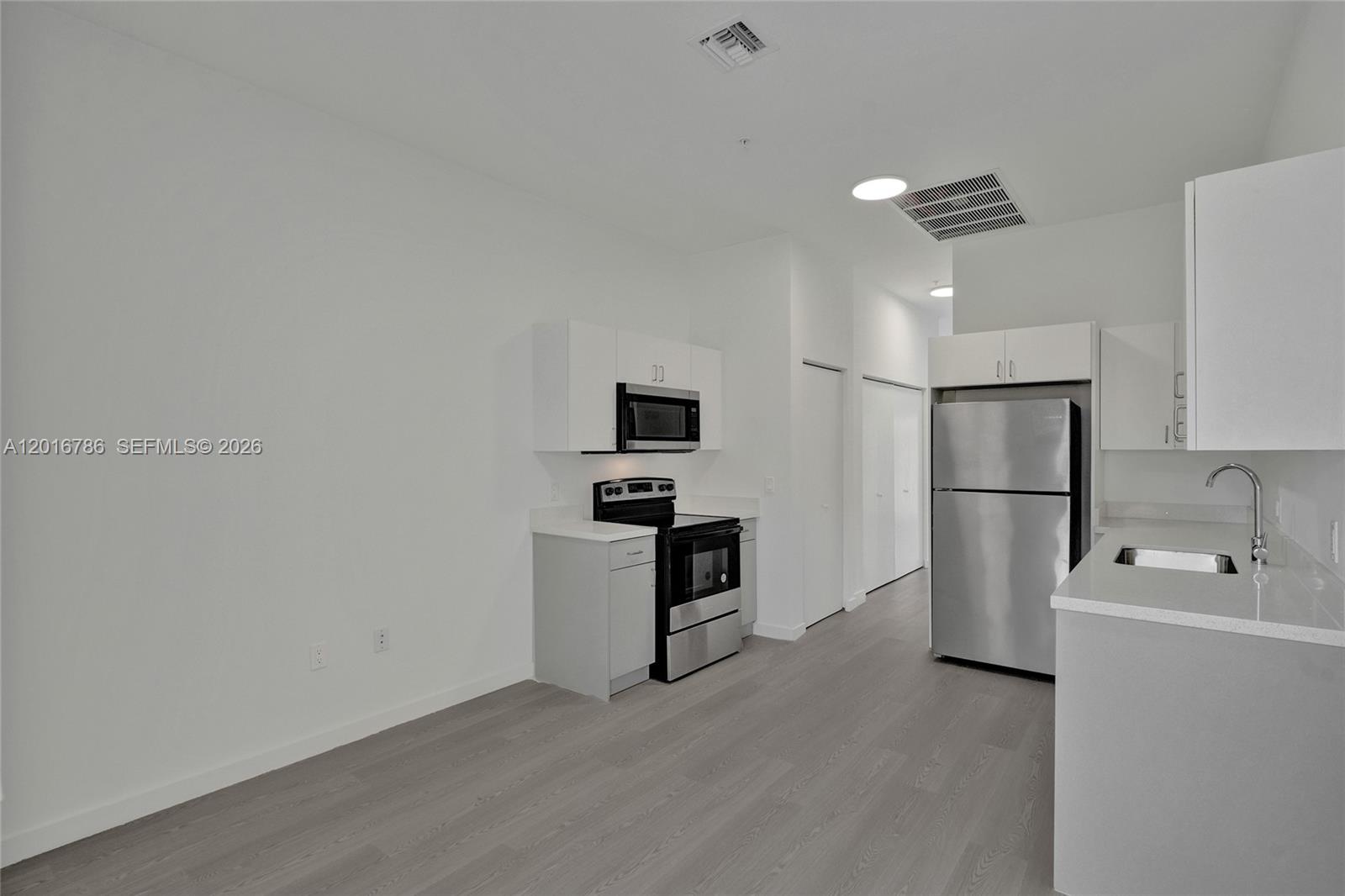 A modern kitchen features white cabinets, stainless steel appliances, and light wood-look flooring — 1567 NW 1st St # 9, Miami FL 33125, MIAMI, FL