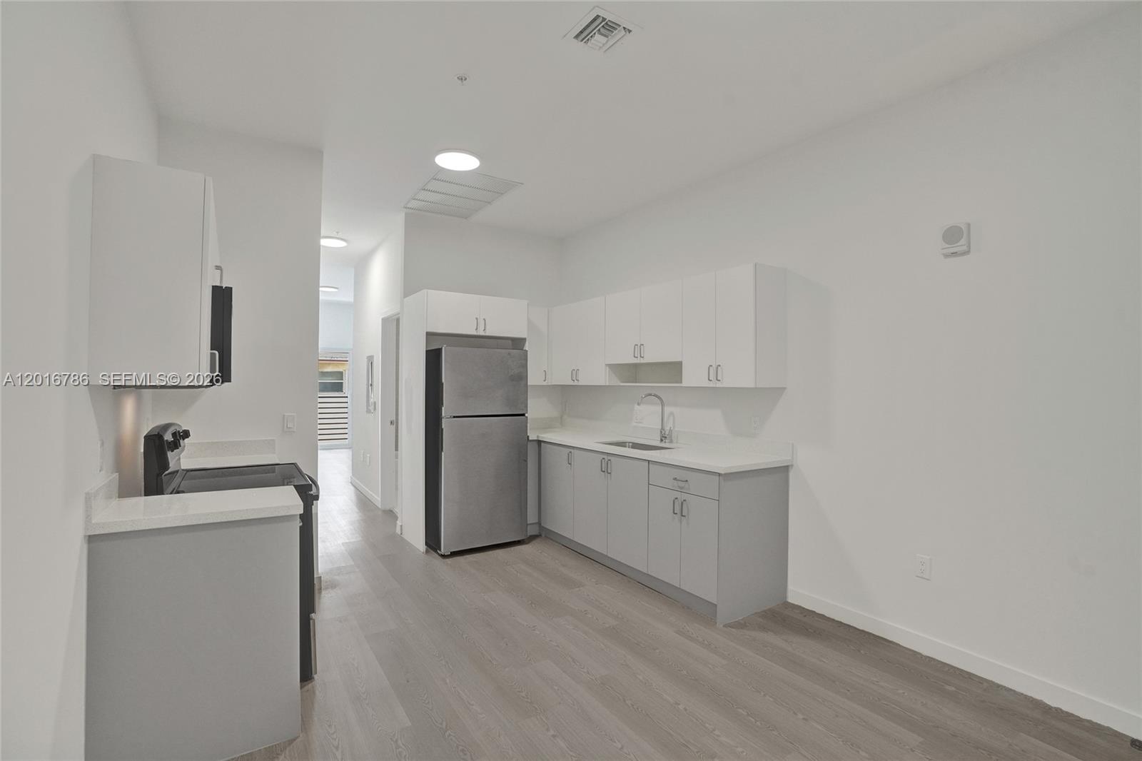 A kitchen features white upper cabinets, grey lower cabinets, stainless steel appliances, and wood flooring — 1567 NW 1st St # 9, Miami FL 33125, MIAMI, FL