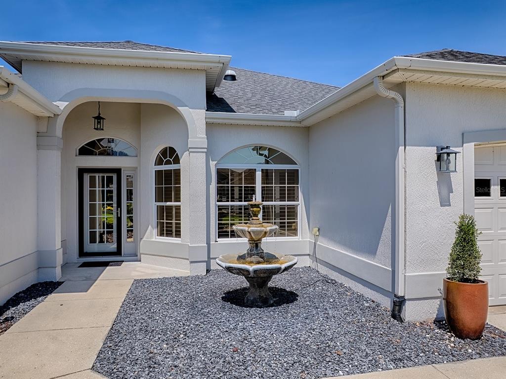 The exterior of a white house features a stone fountain, gravel landscaping, and a front entrance — 1969 HARTFORD PATH, THE VILLAGES, FL