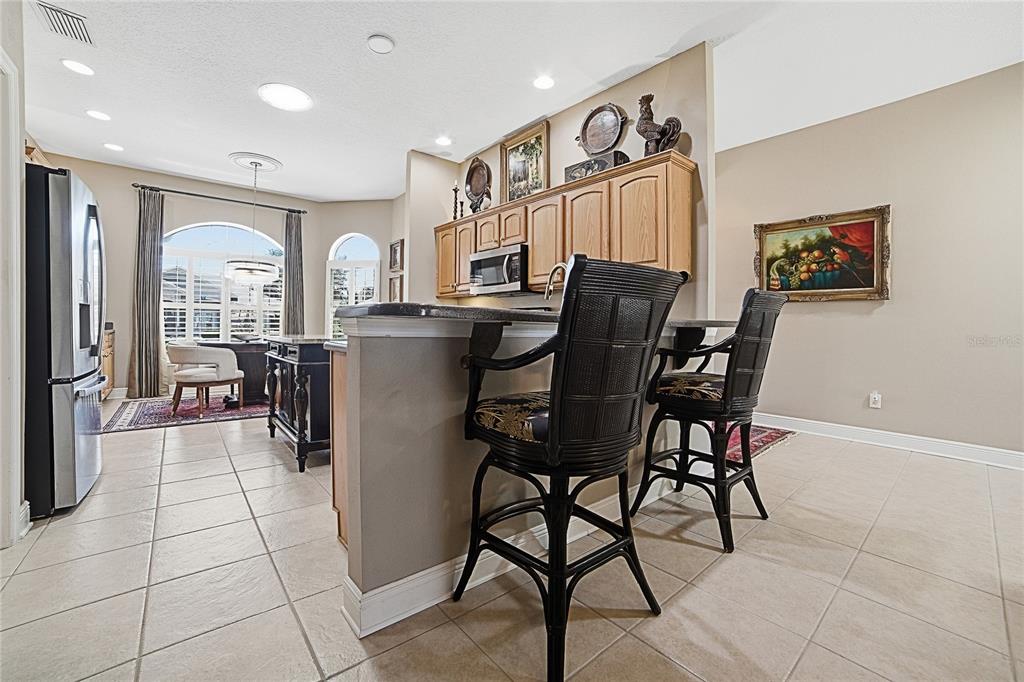 A kitchen with light wood cabinets, a breakfast bar with two black chairs, and tile flooring — 1969 HARTFORD PATH, THE VILLAGES, FL