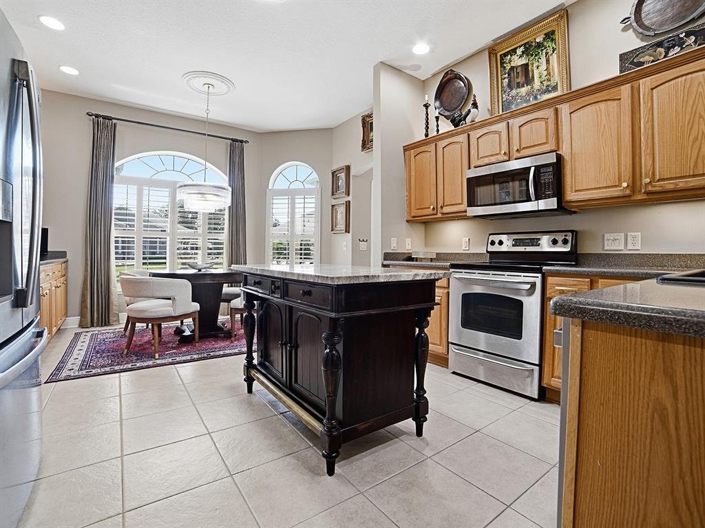 A kitchen features light wood cabinets, a dark wood island, and an adjacent dining area — 1969 HARTFORD PATH, THE VILLAGES, FL