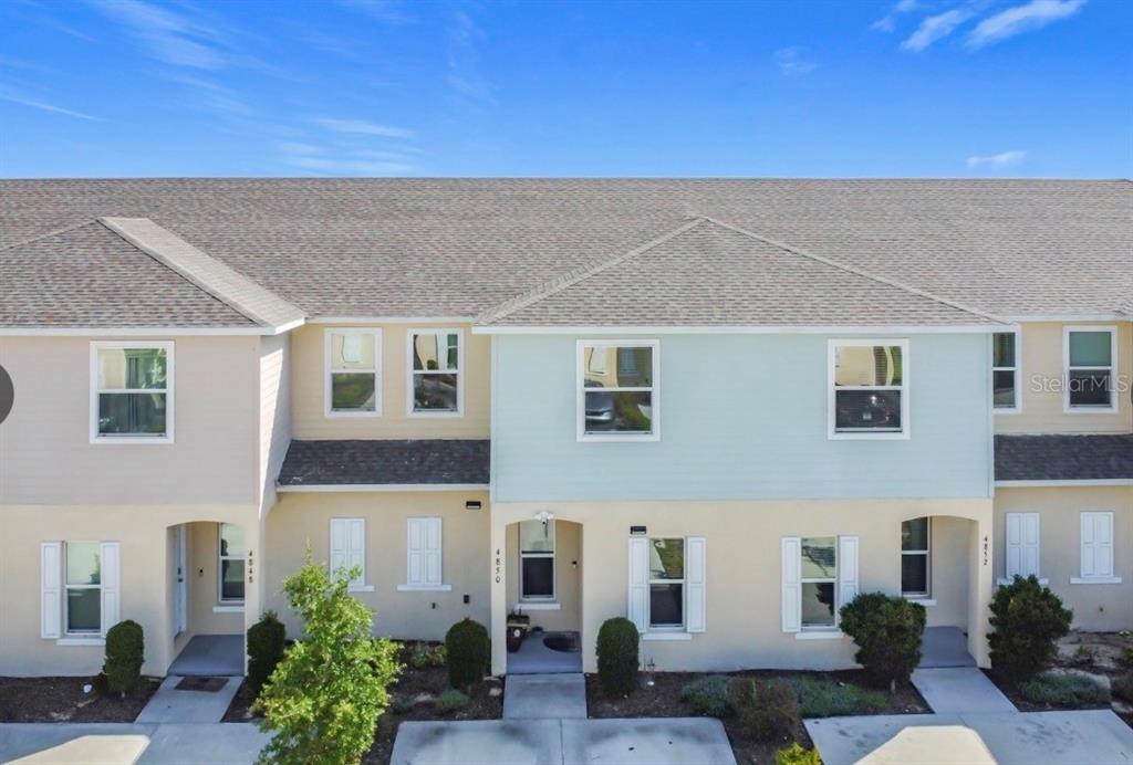 An exterior view of a multi-unit townhouse building with light-colored siding and shingled roofs — 4850 CORAL CASTLE DRIVE, KISSIMMEE, FL