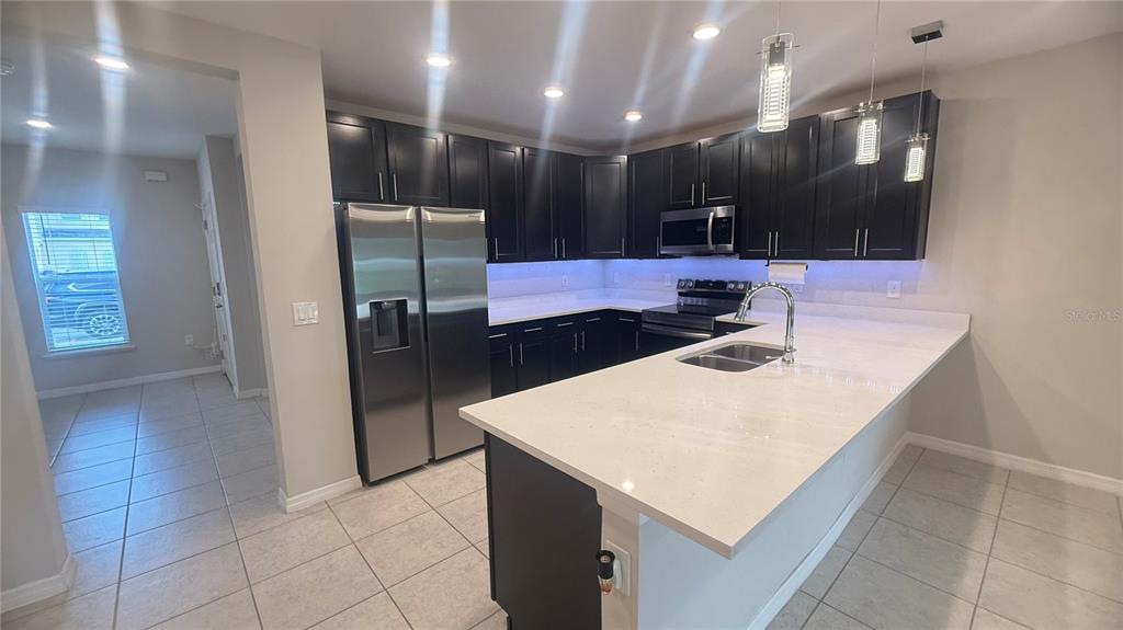 A kitchen features dark cabinets, stainless steel appliances, white countertops, and a breakfast bar — 4850 CORAL CASTLE DRIVE, KISSIMMEE, FL