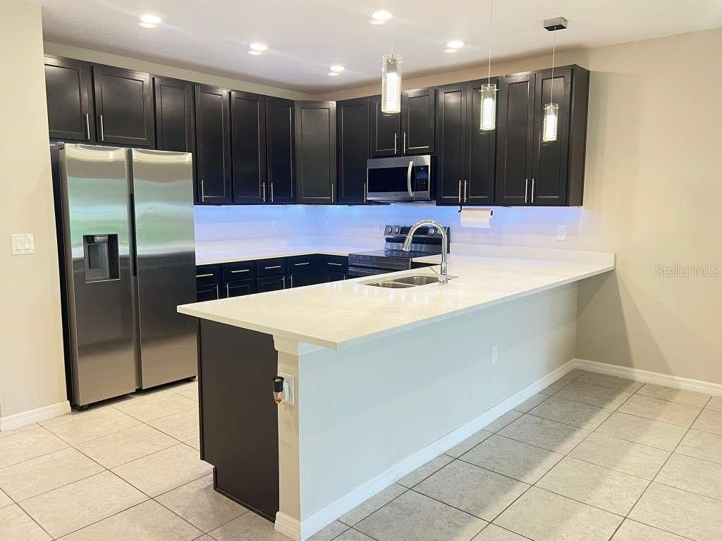 A modern kitchen features dark cabinets, stainless steel appliances, and a white quartz island countertop — 4850 CORAL CASTLE DRIVE, KISSIMMEE, FL