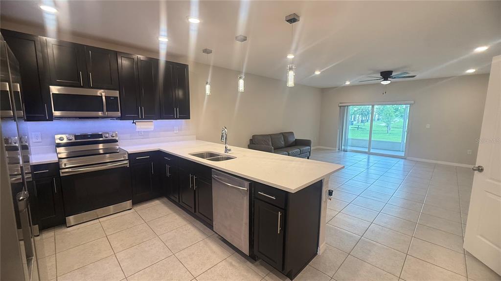A kitchen with dark cabinets and white countertops opens into a living area with tile floors — 4850 CORAL CASTLE DRIVE, KISSIMMEE, FL