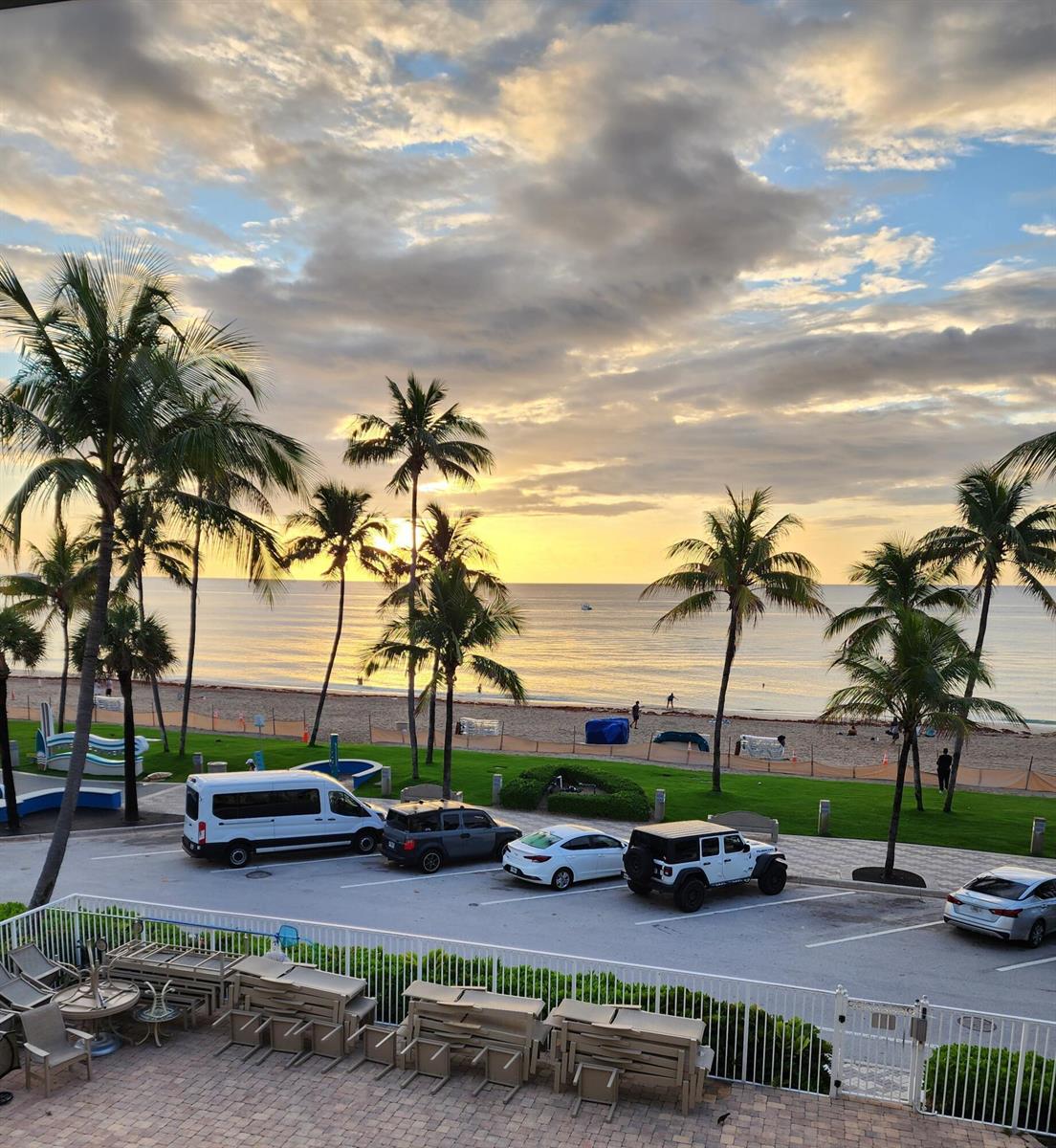 A view of a beach, palm trees, and a parking lot from an elevated patio — 2080 E Hillsboro Boulevard # 108, Deerfield Beach FL 33441, DEERFIELD BEACH, FL