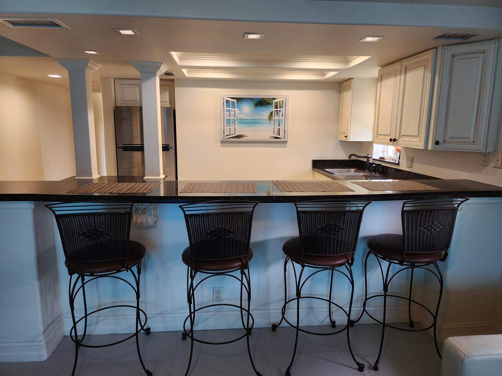 A kitchen features a black countertop breakfast bar with four stools and white cabinetry — 2080 E Hillsboro Boulevard # 108, Deerfield Beach FL 33441, DEERFIELD BEACH, FL