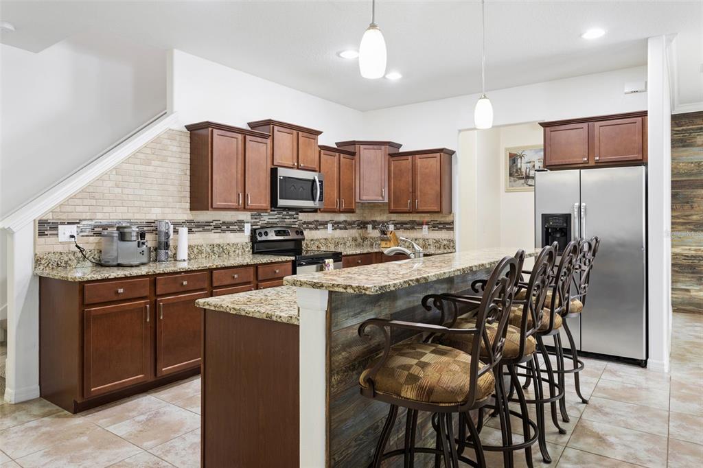 A kitchen features wood cabinets, granite countertops, a breakfast bar, and stainless steel appliances — 20220 POND APPLE LANE, TAMPA, FL