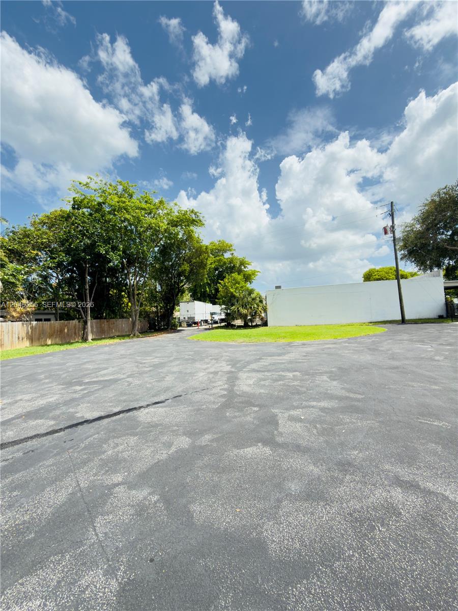 A paved parking lot sits in front of a white wall and green trees — 1601 S 21st Ave, Hollywood FL 33020, HOLLYWOOD, FL