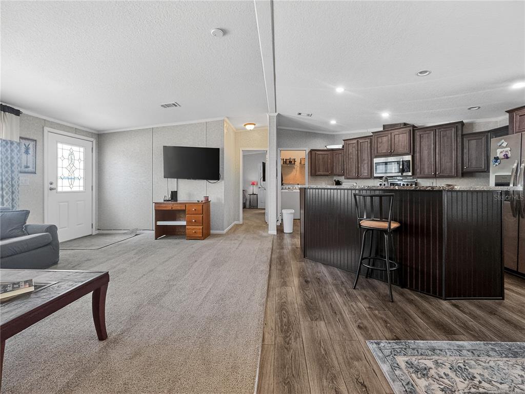 An open-concept living room and kitchen featuring carpeted and wood-look flooring with dark cabinetry — 9925 SCEPTER AVENUE, BROOKSVILLE, FL