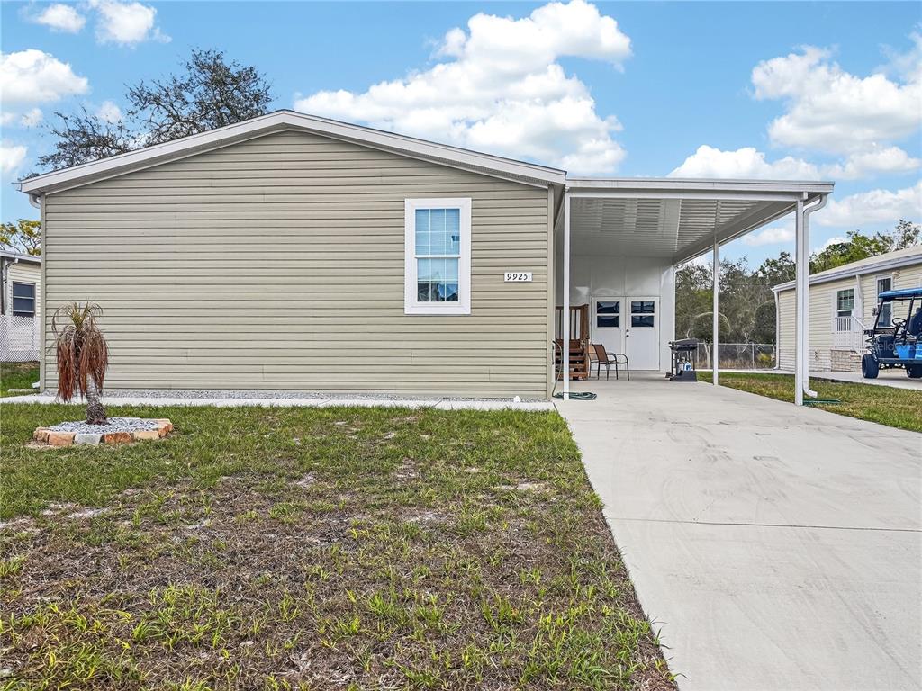 A light-colored mobile home features a concrete driveway, a carport, and a small front yard — 9925 SCEPTER AVENUE, BROOKSVILLE, FL