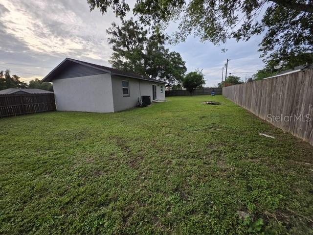 A view of a backyard with a gray house, a wooden fence, and green grass — 6881 NW 14TH AVENUE, OCALA, FL