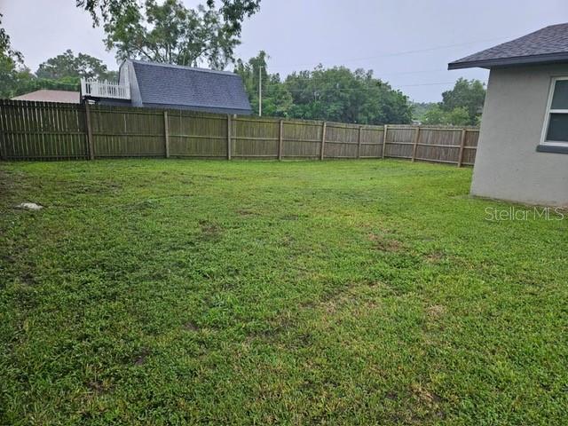 A grassy backyard features a wooden privacy fence and a view of a neighboring house — 6881 NW 14TH AVENUE, OCALA, FL