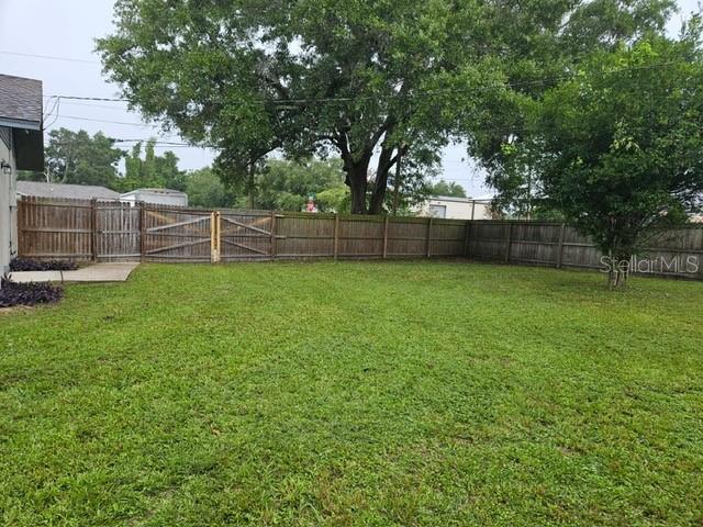A grassy backyard features a wooden privacy fence and a large mature tree — 6881 NW 14TH AVENUE, OCALA, FL