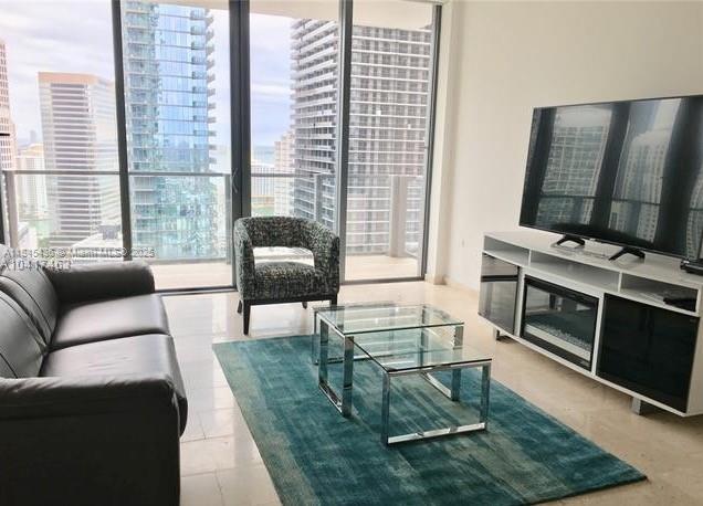 A living room features a dark leather sofa, a glass coffee table, and city views — 88 SW 7th St # 2603, Miami FL 33130, MIAMI, FL