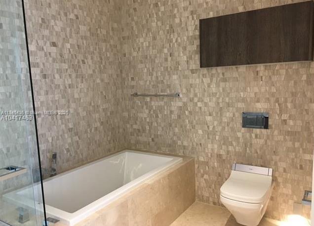 A bathroom features a white bathtub, a wall-mounted toilet, and textured stone wall tiles — 88 SW 7th St # 2603, Miami FL 33130, MIAMI, FL