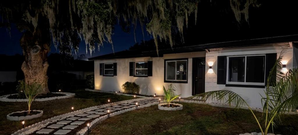 A single-story house at night with a stone walkway, exterior lighting, and a large tree — 1000 E DIXIE AVENUE, LEESBURG, FL