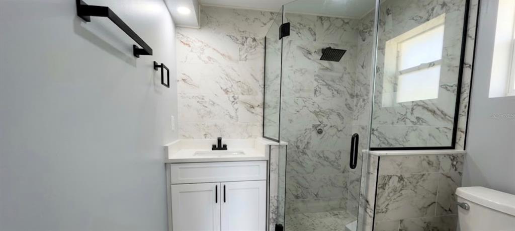 A bathroom features a white vanity, a glass-enclosed shower with marble-look tile, and a toilet — 1000 E DIXIE AVENUE, LEESBURG, FL